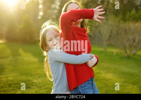 Due graziosi sorelle ingannare intorno insieme sull'erba su una soleggiata giornata estiva. I bambini di essere sciocco e divertirsi. Tempo per la famiglia. Foto Stock