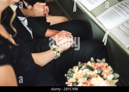 Formale persone vestite seduti sulle palle in chiesa. Primo piano di mani uomo e donna aggrappate. Coppia amorevole in chiesa. Foto Stock