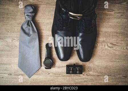 Abiti da uomo con scarpe in pelle nera formale, cravatta, orologi e gemelli vista dall'alto, piatto su sfondo tavola in legno. Foto Stock