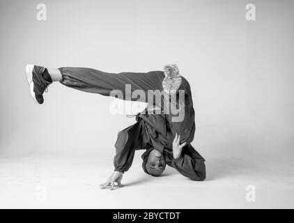 Un ballerino o bboy hip hop uomo si congela in una posa su uno sfondo bianco. Bboy che fa acrobazie eleganti. Foto Stock