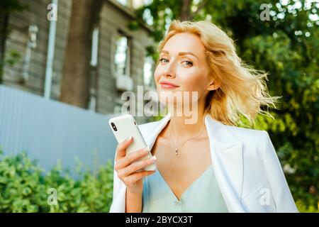Foto closeup di una bella donna di affari con uno smartphone che indossa abiti bianchi e sorridere alla fotocamera Foto Stock