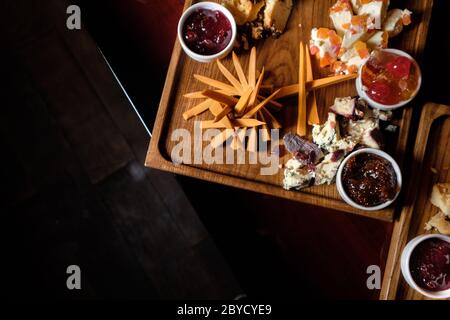 Una vista dall'alto di una piastra di legno con vari formaggi e marmellata, tagliata a piccoli pezzi sullo sfondo del tavolo, piatto Foto Stock