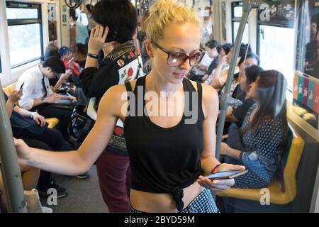 Viaggiatore caucasico femminile utilizzando il telefono cellulare sulla metropolitana di trasporto pubblico a Kuala Lumpur, capitale della Malesia Foto Stock