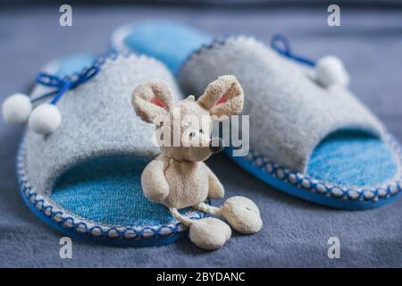 Un mouse giocattolo si trova sulle pantofole con i pompon in piedi su un tappeto soffice. Abbigliamento e scarpe per donne o bambini. Il concetto di calore domestico. Foto Stock