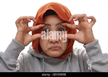 Stanca donna musulmana apre gli occhi con un dito, cercando di rimanere sveglio, primo piano ritratto isolato su bianco Foto Stock