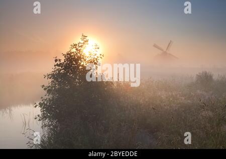 sole del mattino e mulino a vento in nebbia fitta Foto Stock