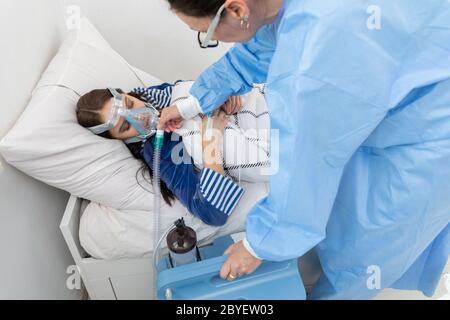 Il medico controlla il collegamento del ventilatore. L'adolescente si trova su un letto d'ospedale. Maschera di ossigeno sul tratto respiratorio. Foto Stock