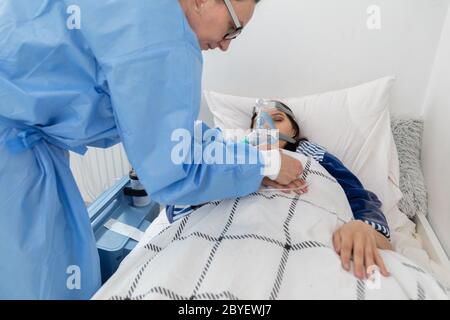 Il medico controlla il collegamento del ventilatore. L'adolescente si trova su un letto d'ospedale. Maschera di ossigeno sul tratto respiratorio. Foto Stock