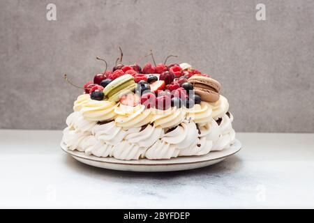 Torta di meringa al Pavlova grande con frutti di bosco freschi e macaroon su fondo grigio chiaro. Spazio di copia. Foto Stock