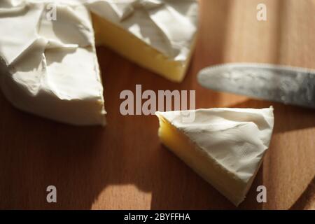 Fetta di formaggio Camembert e intera con l'estremità coltello su una tavola di legno Foto Stock