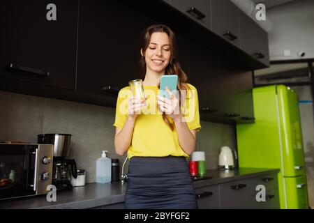 Donna dall'aspetto bello con un bicchiere d'acqua e uno smartphone Foto Stock