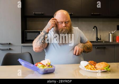 Uomo grande adulta tatuato guardando attentamente al cibo Foto Stock