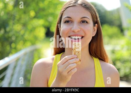 Donna felice di idoneità che tiene un'energia bar. Primo piano di ragazza sportiva che mangia uno spuntino di cereali all'aperto. Foto Stock