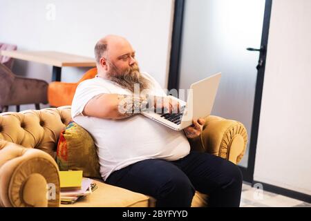 Uomo baldeggiato in groppa seduto con un computer portatile in mani e lavorando online Foto Stock
