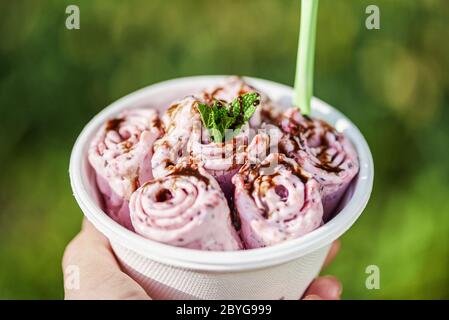 Gelato alle bacche arrotolate con foglie di menta, dessert gelato fatto a mano. Gelato con mano. Foto Stock