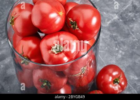 Pomodori grandi freschi su sfondo grigio. Pomodori interi e affettati hanno sparato il primo piano con meta per il testo. Pomodori Art Concept nel bicchiere. Foto Stock