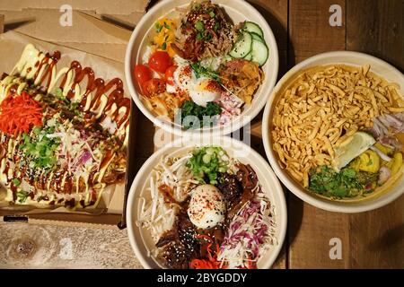 Manzo e pollo su riso in stile coreano serviti con Okonomiyaki (pancake giapponesi) e Khao Soi, zuppa di noodle al curry della Tailandia del Nord Foto Stock