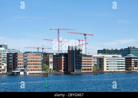 Moderni edifici residenziali nel porto urbano con gru sullo sfondo, mentre nuovi edifici sono costruiti. Giornata di sole con cielo blu. Foto Stock