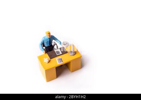Uomo d'affari in miniatura seduto dietro la sua scrivania. Macro ripresa dall'alto del concetto di business delle piccole persone. Foto Stock