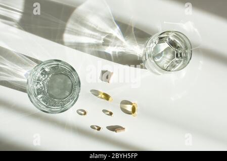 Un bicchiere d'acqua e pillole su un tavolo bianco. Omega 3 capsule di olio di pesce e vitamina D con raggi solari e sole Foto Stock