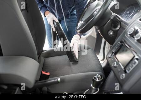 Donna che pulisce il sedile del conducente, pulendolo e aspirandolo per la polvere. Foto Stock