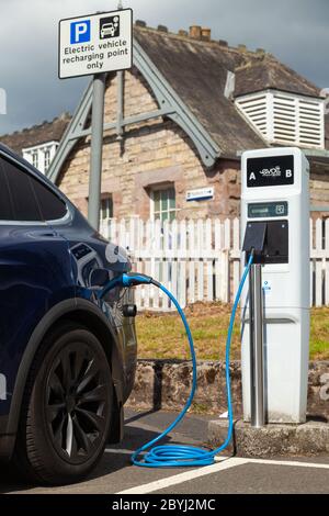 Un'auto elettrica Tesla in carica presso una stazione di ricarica pubblica ad Aberdour, Fife, Scozia Foto Stock
