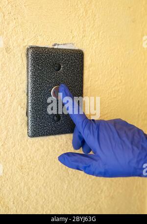 Mano nel guanto premendo il pulsante dell'elevatore. Foto Stock