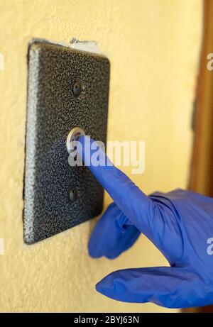 Mano nel guanto premendo il pulsante dell'elevatore. Foto Stock