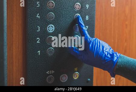 Mano nel guanto premendo il pulsante dell'elevatore. Foto Stock