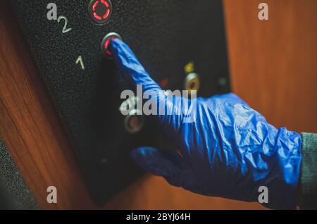 Mano nel guanto premendo il pulsante dell'elevatore. Foto Stock