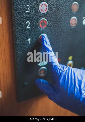 Mano nel guanto premendo il pulsante dell'elevatore. Foto Stock