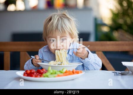 Carino bambino, biondo bambino, mangiando spaghetti in giardino in estate Foto Stock