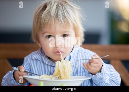 Carino bambino, biondo bambino, mangiando spaghetti in giardino in estate Foto Stock