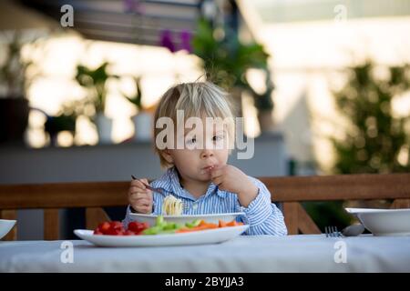 Carino bambino, biondo bambino, mangiando spaghetti in giardino in estate Foto Stock