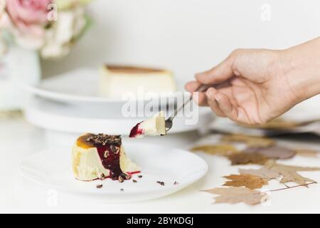 Mano con forchetta mangiare basco cheesecake bruciato con salsa di frutti di bosco mista. Foto Stock