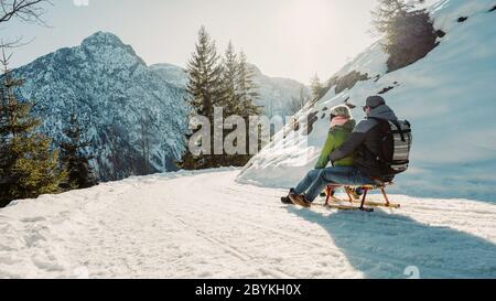 Velocità in discesa su slitta di legno. Felice influencer coppia divertirsi con legno vintage slitta su neve alta montagna - giovani pazzi persone Foto Stock