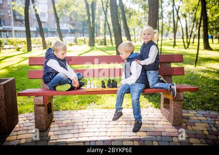 I bambini piccoli che giocano a scacchi nel parco sulla panchina. Vacanze estive, giochi intellettuali. Scacchi club per bambini. Felice infanzia e bambini Foto Stock