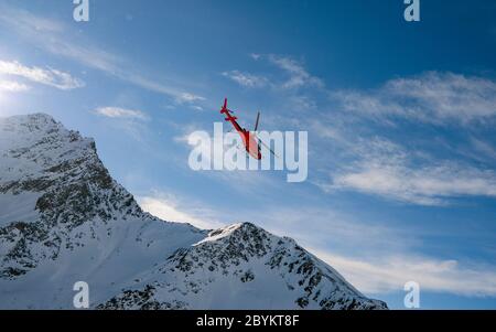 Elicottero di soccorso rosso che sorvola la vista delle rocce innevate nella località sciistica alpina di Zermatt vicino al monte Cervino. Paesaggio naturale invernale della Svizzera Foto Stock