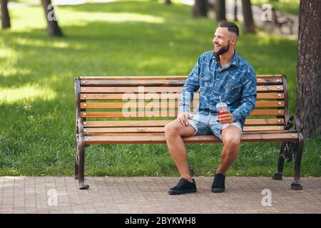 Un ragazzo con limonata riposa in un parco su una panchina in primavera. Giorno di sole. Foto Stock