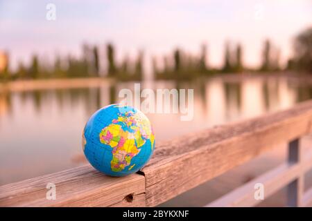 Piccolo mondo globo posto sulla recinzione di legno di un grande lago. Concetto di viaggio e cura del pianeta. Foto Stock