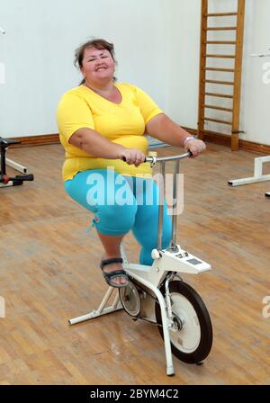 Il sovrappeso donna esercita sul simulatore di bici Foto Stock