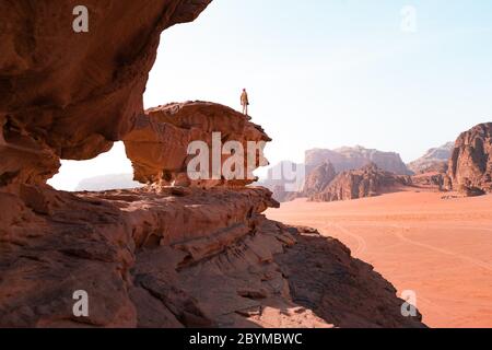 Il giovane è in cima alla scogliera. Wadi Rum, conosciuta anche come la Valle della Luna, è una valle tagliata nella pietra arenaria e nella roccia granitica nel sud della Giordania Foto Stock