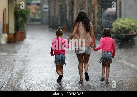 25.07.2017, Orvieto, Umbria, Italia - Donna che cammina su una strada in tempo piovoso con due ragazze a portata di mano. 00S170725D077CAROEX.JPG [VERSIONE MODELLO: NO, PR Foto Stock