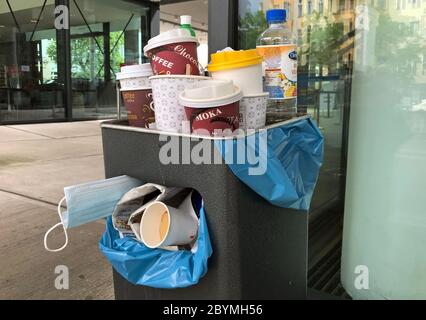 29.04.2020, Berlino, , Germania - tazze di caffè vuote, bottiglie di bevande e protettori per bocca e naso stanno attaccando da una bidone di rifiuti troppo pieno. 00S20042 Foto Stock