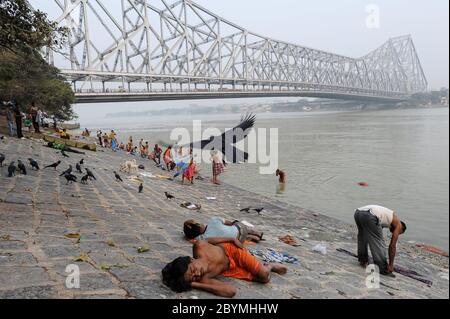 01.12.2011, Calcutta, Bengala Occidentale, India - la gente sulle rive del fiume Hugli con il ponte Howrah sullo sfondo, che collega i due cit Foto Stock