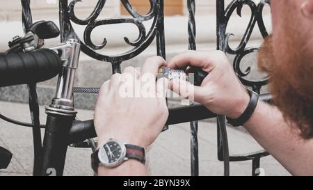 Primo piano di un giovane uomo che blocca la sua bicicletta vintage sulla strada della città con lucchetto Foto Stock