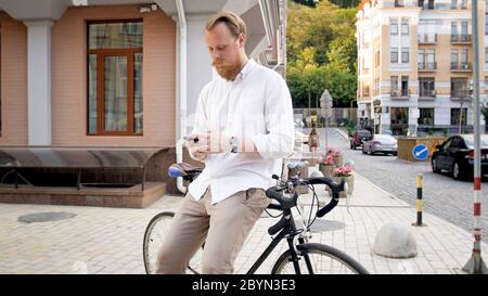 Giovane e alla moda che pende sulla bicicletta e digita un messaggio sullo smartphone Foto Stock