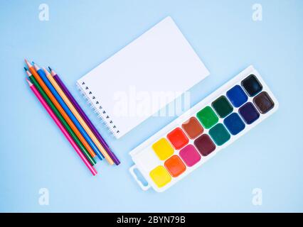 Matite colorate, notebook, pennello e acquerelli su sfondo blu con copyspace. Piatto stile di laici. Si torna a scuola concetto. Foto Stock