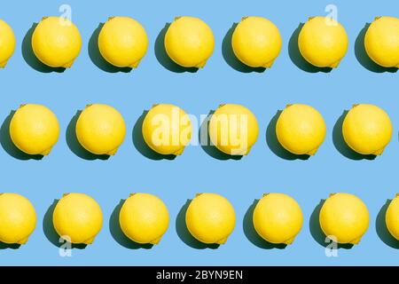 Ripetizione di un motivo fotografico continuo di limoni gialli interi freschi su sfondo blu. Struttura del cibo. Foto Stock