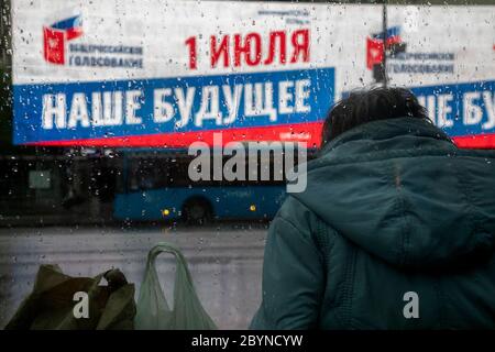 Mosca, Russia. 10 giugno 2020 UNA donna attende un autobus presso una fermata dei mezzi pubblici in via New Arbat sullo sfondo di un banner pubblicitario sul voto interamente russo sulle modifiche alla Costituzione della Federazione russa il 1 luglio 2020, nel centro di Mosca, Russia. Il banner recita '1 luglio. Il nostro futuro" Foto Stock